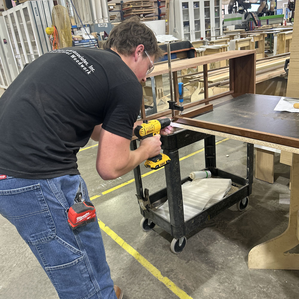 Craftsman using a power drill on a woodworking project in a production facility, showcasing Schlaegle Design Build's commitment to quality craftsmanship and custom woodworking services.